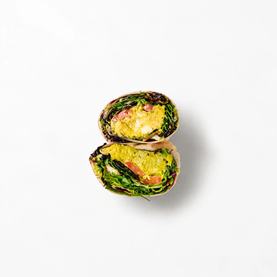 Halved vegetable wraps stacked to reveal leafy greens, avocado spread, and tomato filling on a white background.