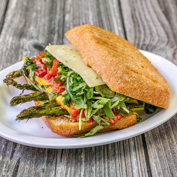 Bertha's Cafe's panini with asparagus, roasted red peppers, arugula, and cheese on a white plate.
