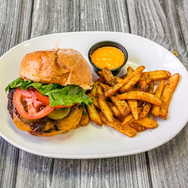 Bertha's Cafe burger with cheese, lettuce, tomato, pickles, and a side of seasoned fries and dipping sauce.
