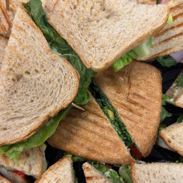 Overhead view of various sandwiches and paninis with fresh lettuce, cut into triangles, on a dark tray.