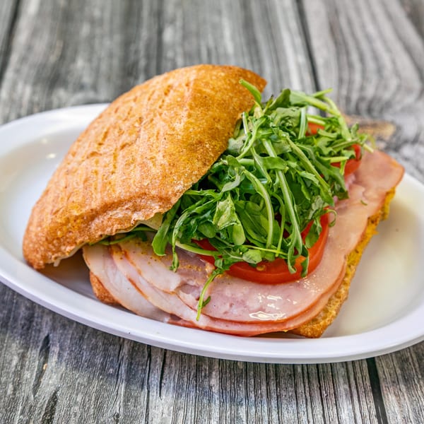 A Bertha's Cafe sandwich with turkey, tomatoes, and arugula on a white plate.