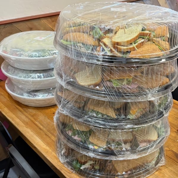 Stacked catering trays of sandwiches and salads, wrapped in plastic, from Bertha's Cafe.