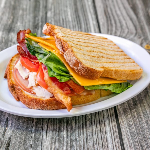 A Bertha's Cafe & Catering club sandwich with turkey, bacon, lettuce, tomato, and cheese on toasted bread.