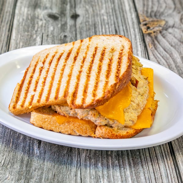 A Bertha's Cafe grilled cheese sandwich with tuna salad and melted cheddar on a white plate.