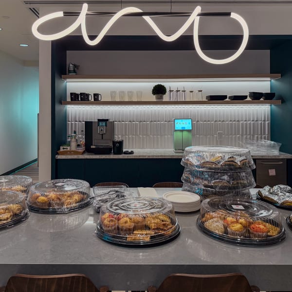 Bertha's Cafe counter with multiple platters of pastries and muffins, coffee machine, and modern lighting.