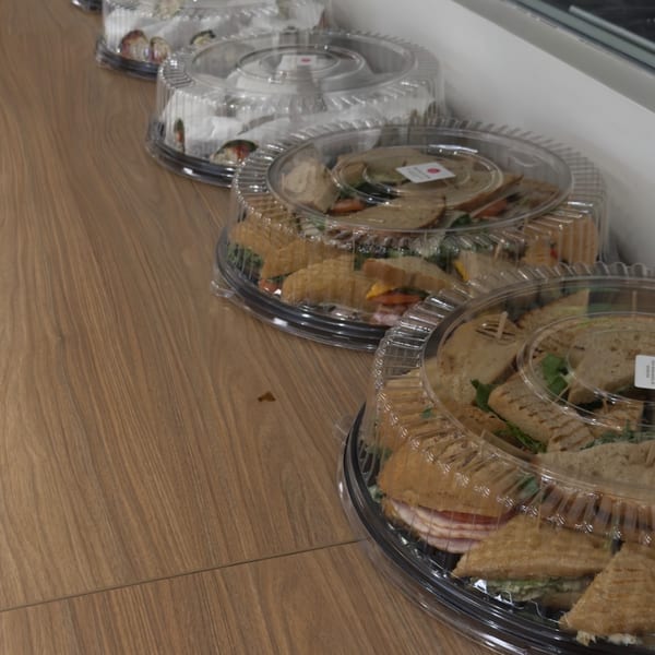 Multiple catering trays of sandwiches and wraps from Bertha's Cafe & Catering on a wooden surface.