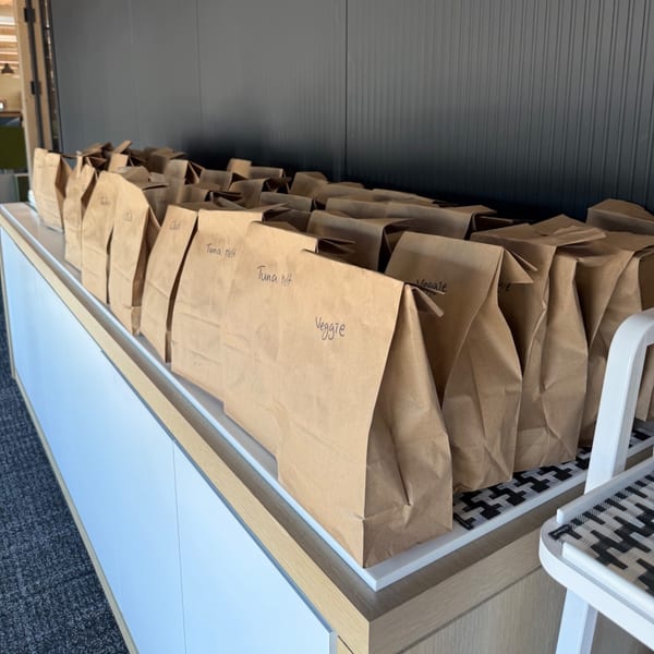 Rows of Bertha's Cafe & Catering brown paper lunch bags with handwritten labels like "Tuna Melt" and "Veggie".