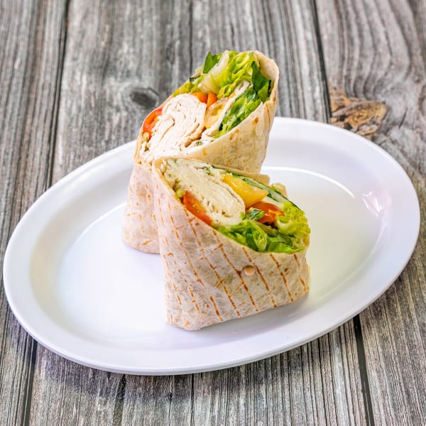 Two halves of a chicken and vegetable wrap on a white plate, against a rustic wooden background.