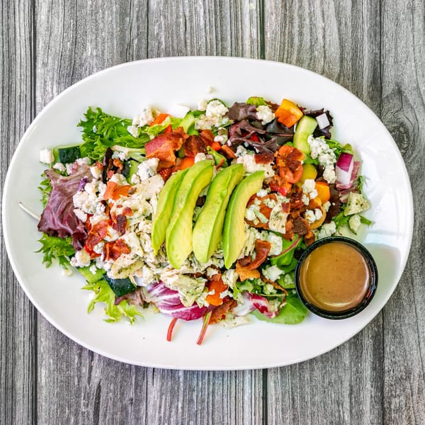 Bertha's Cafe & Catering's Cobb salad with avocado, bacon, blue cheese, and dressing on a white plate.