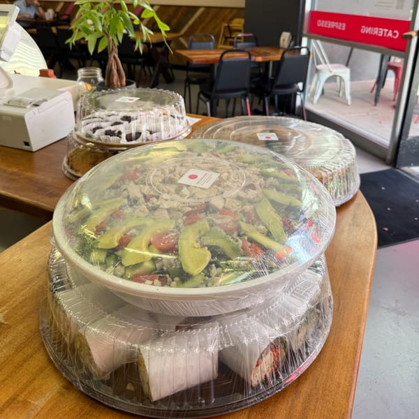 Catering display at Bertha's Cafe with a large salad, wraps, and cakes on a wooden counter.