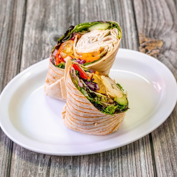Two Bertha's Cafe wraps, filled with turkey, lettuce, and colorful vegetables, on a white plate.