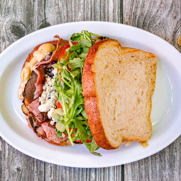 Open-faced Bertha's Cafe sandwich with roast beef, blue cheese, arugula, and tomatoes on toast.